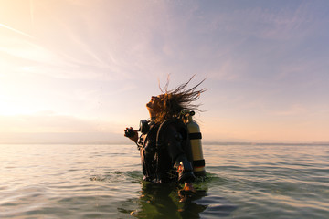 Female Scuba Dive Instructor Wearing a Dry Suit, a Twin Tank and Holding Fins Flipping Wet Hair in...