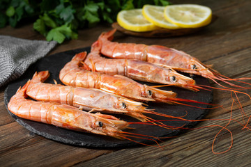 Large langoustines on a black plate on a brown wooden table. Seafood for a healthy diet