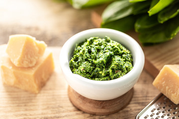 Wild leek pesto with olive oil and parmesan cheese in a white ceramic mortar on a wooden table. Useful properties of ramson.