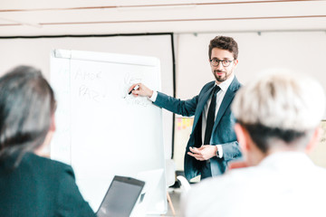 Smiling speaker in eyeglasses talking to colleagues. Group of workers discussing presentation of new project at briefing. Business meeting concept