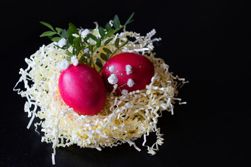 Red Easter eggs in a decorative basket nest with leaves and flowers on black background. Easter greeting card.