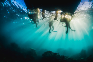 Underwater silhouette shot of scuba divers and a dive boat with golden sun rays shining through the...