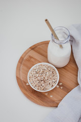 Non dairy alternative vegan oat milk in bottle with bamboo eco zero waste straw and fresh oats on wooden tray. Gluten and lactose free products.