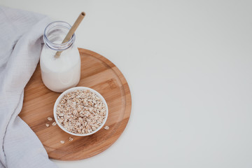 Non dairy alternative vegan oat milk in bottle with bamboo eco zero waste straw and fresh oats on wooden tray. Gluten and lactose free products.