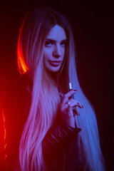 Fashion portrait of beauty model woman in bright lights smoking e-cigarette. tobacco heating system