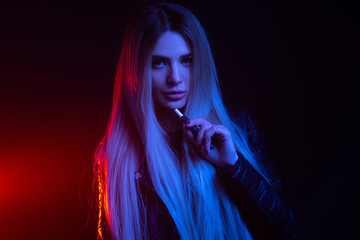 Fashion portrait of beauty model woman in bright lights smoking e-cigarette. tobacco heating system