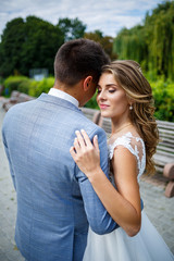 Young stylish guy in a suit the groom and the bride beautiful girl in a white dress with a train walk in the park on their wedding day