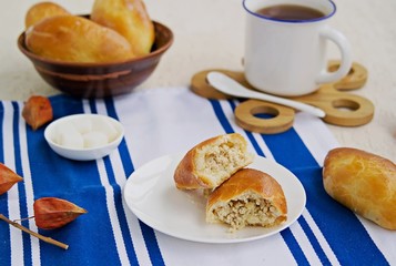Homemade baked pies from yeast dough with meat on a white plate on a light concrete background. Russian kitchen. Homemade baking.