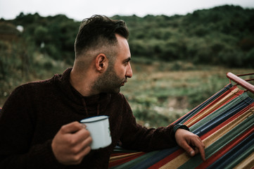 Caucasian Armenian man with bristle on his face is sitting and having rest in the colorful hammock...