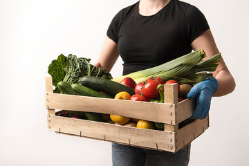 The supplier in protective gloves holds a wooden shopping basket with purchases. Brown background of wooden boards. Health protection against covid-19  © Aldi