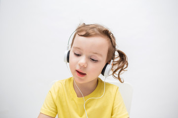 a girl on a white background in a yellow t-shirt. the little girl listens to music through headphones.