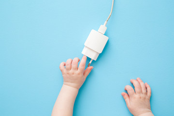 Baby hands exploring white charging phone cable with plug on light blue table background. Pastel color. Close up. Point of view shot. Top down view.