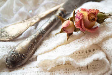 old silver fork with knife over the white vintage napkin and dry roses