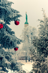New Year's red balls on the branches of spruce with snow in the center of winter Riga. Against the background of the national monument of freedom of Latvia