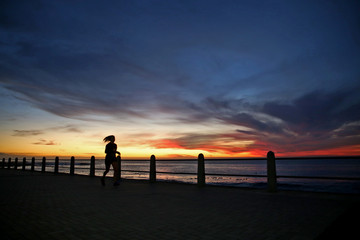 Silhouetted sportswoman training for fitness by running on seaside promenade at sunset 