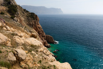 Fototapeta na wymiar The turquoise sea and cliff top view of the Crimean coast, the tourist season, the trip to the Crimea, stone shore and beach
