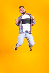 Fototapeta na wymiar Young handsome man with facial hair jumping over yellow wall with a lot of copy space for text. Portrait of confident bearded male, wearing fashionable casual outfit. Isolated, background.