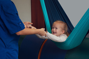 girl enjoying a sensory therapy on a hammock while physiotherapist assisting her