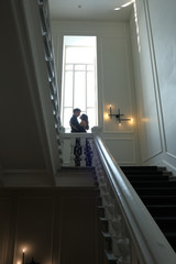 Young beautiful couple - a girl and a guy are standing or sitting on a white staircase inside a large beautiful building. 