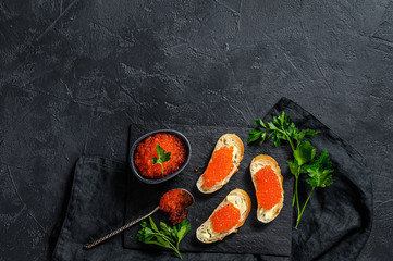 Red caviar in bowl and Sandwiches on stone board. Black background. Top view. Copy space