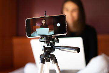 Mobile on a tripod recording a female vlogger at home.