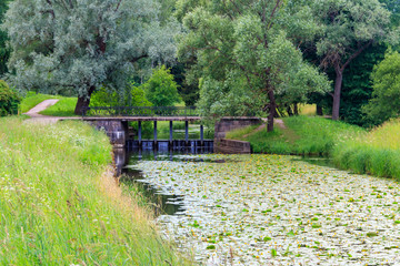 Fototapeta premium Black bridge-dam over the Slavyanka river in Pavlovsk park, Russia