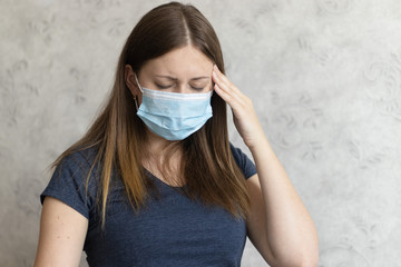 Young unhappy woman in medical face mask has headache. The girl feels pain, symptoms of the...