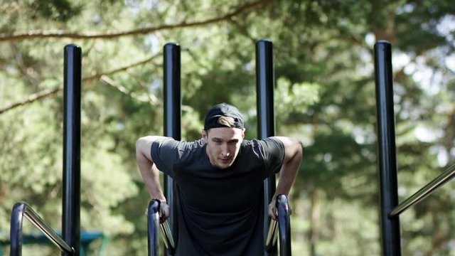 Adult caucasian strong athlete is doing an physical exercise on bars at the gym ath the park