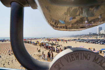 Blick auf einen dicht bevölkerten Sandstrand mit Spiegelung in einem Münzfernrohr