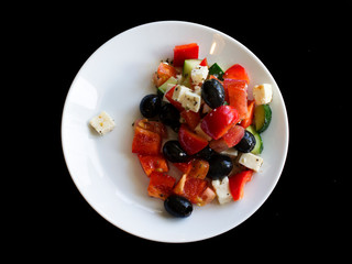 fresh greek salad in white plate on black table. vegetable salad with feta cheese. healthy food.