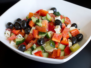 fresh greek salad in white plate on black table. vegetable salad with feta cheese. healthy food.