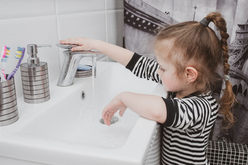 Cute girl in striped clothes washes his hands with soap. Pandemic Hygiene Concept