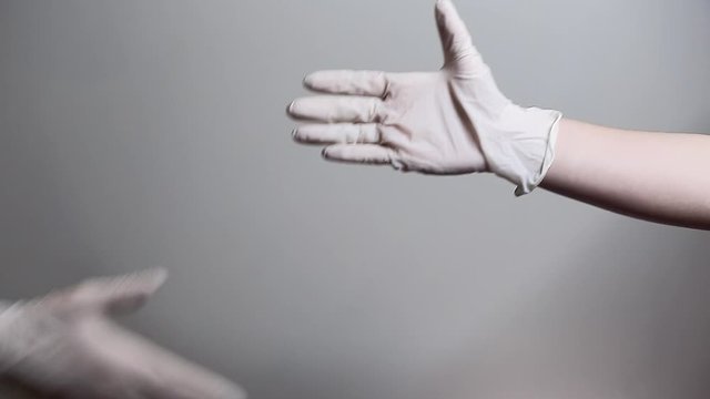 Two people put on latex gloves in order to shake hands safely during the pandemic. 24FPS HD.