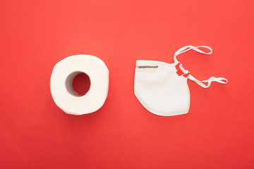 top view of white clean toilet paper roll and safety mask on red background