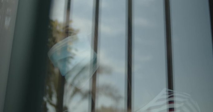 Mujer mirando a trav&eacute;s de la ventana con una mascarilla durante la pandemia del Covid-19 o Coronavirus