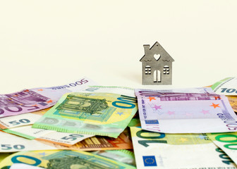 Mortgage, savings, own real estate concept. A track of money leads to buying a home. House and cash euro banknotes on a pastel yellow background. Copy space