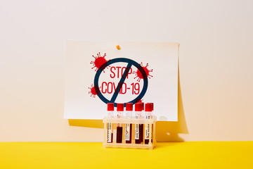 paper with stop covid-19 lettering near test tubes with coronavirus test on white and yellow