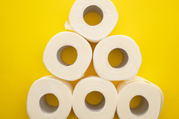 top view of white toilet paper rolls arranged in pyramid on yellow background