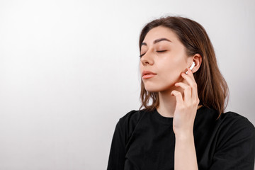 young brunette woman in a black t-shirt on a white background listens to music isolated