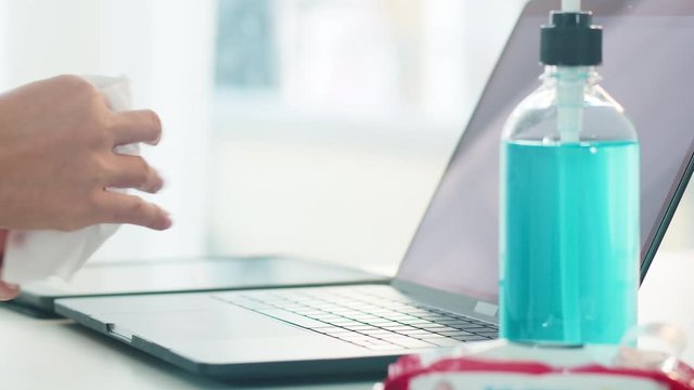 Asian woman using alcohol spray on tissue clean laptop before open for protect coronavirus. Female clean computer for hygiene when social distancing stay at home and self quarantine time.