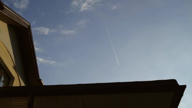 Plane flies far away in sky above house