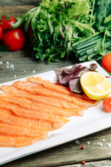 Restaurant dish with vegetable decor on a wooden background. Salted salmon cut into slices on a plate.