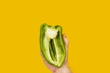 Mano sosteniendo un pimiento verde cortado por la mitad sobre un fondo amarillo aislado. Vista de...