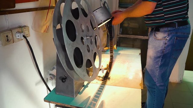 CU: movie technician puts film reel on large spool to show old picture with vintage cinema equipment in projection booth closeup