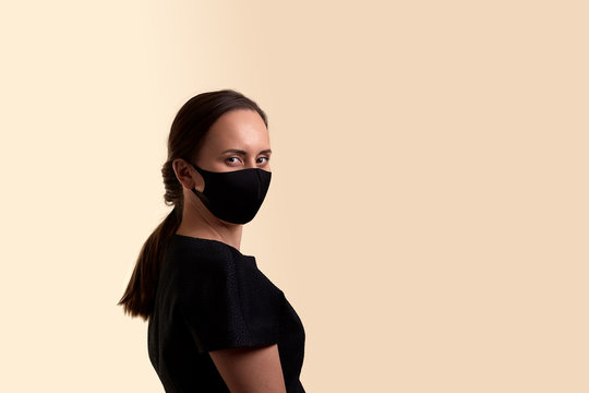 Woman In Black Dress And Black Face Mask Looking At Camera Over His Shoulder Half A Turn