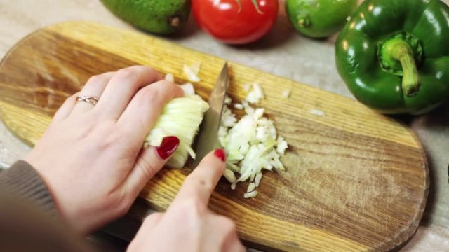 Dicing white onion on chopping board with veggies around