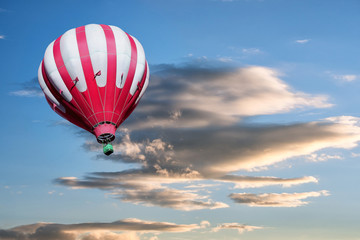 Red and white hot air balloon on the background of bright rosy sunset.