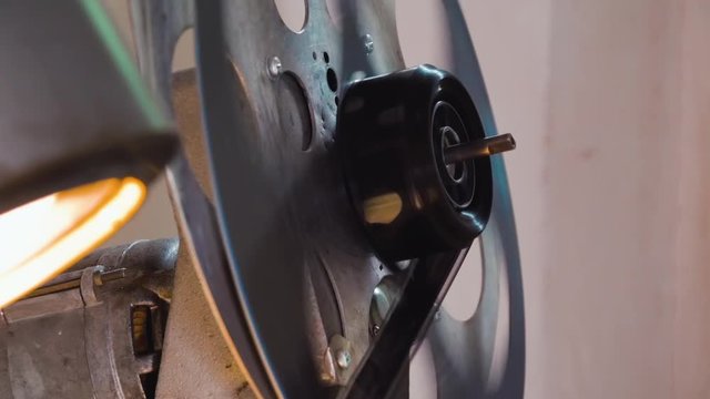 CU: large metal spool with black film reel rotates by old cinema equipment to show movie in projection booth close view