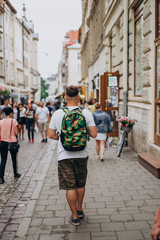 A man with a backpack on a city tour in the summer. A young man walks the city on a sunny day. Sports guy in shorts and with a colored backpack.