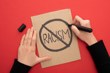 cropped view of woman writing stop racism sign with marker on carton placard on red background